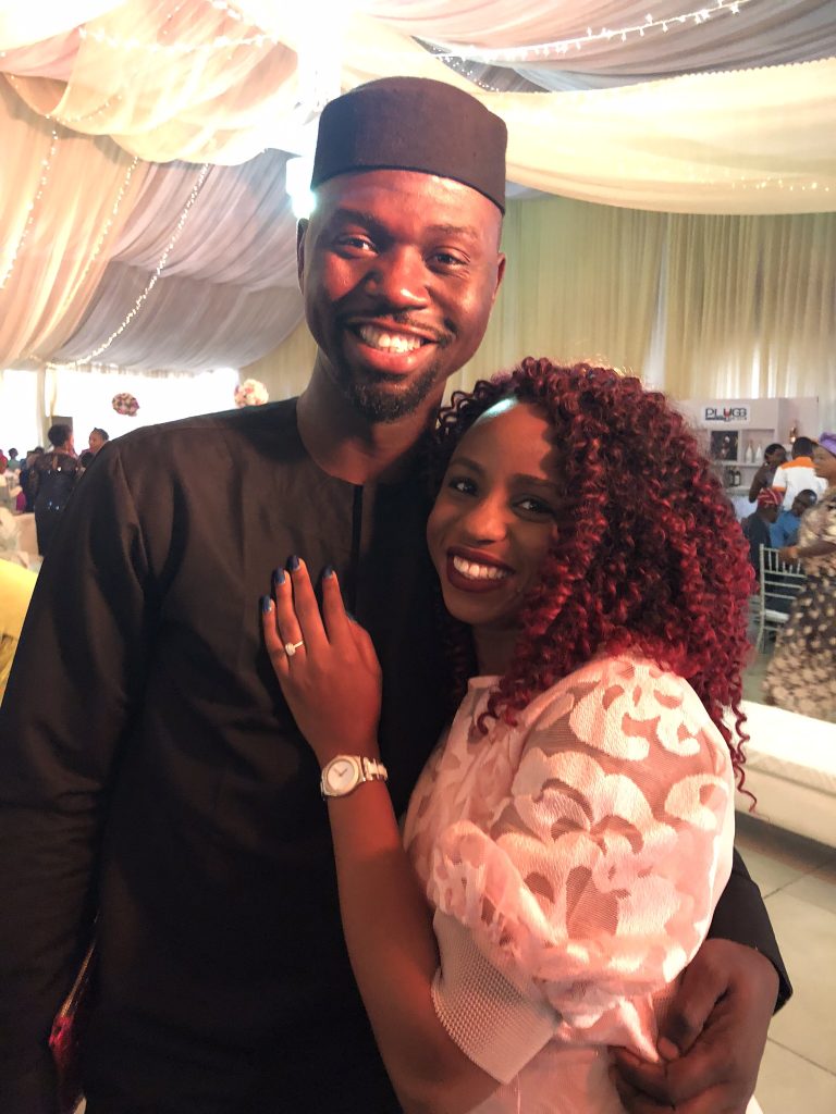 Kemi and Pelu smiling into the camera with Kemi's hand on Pelu's chest