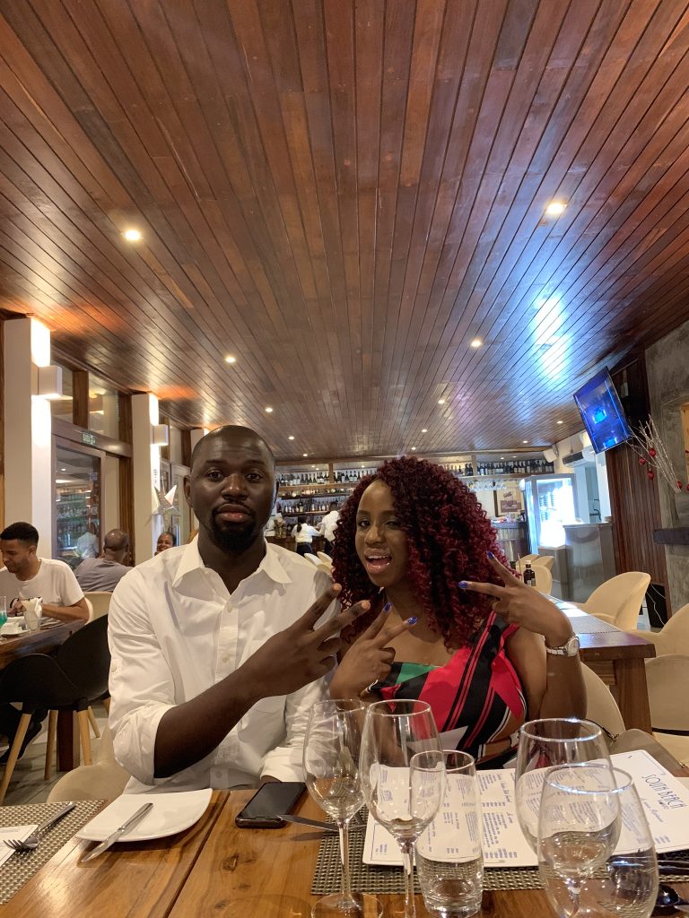 Kemi and Pelu doing the peace sign at a dinner table (just before he proposed) 